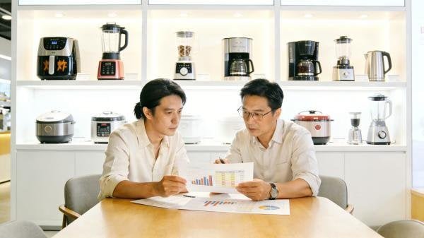 A buyer and a supplier discussing a pricing chart in a factory meeting room.